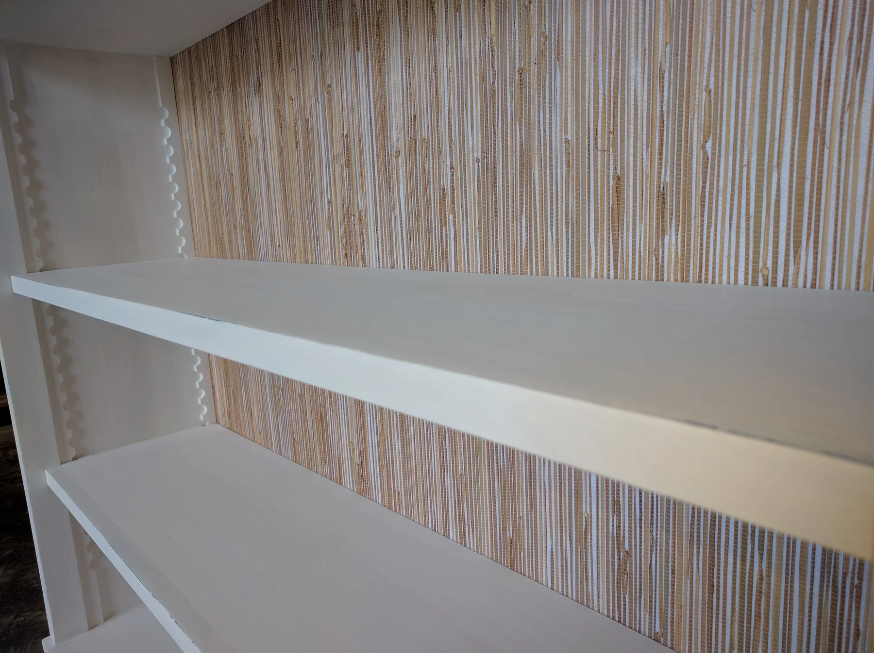 Close view of an adjustable painted shelf against a grasscloth back